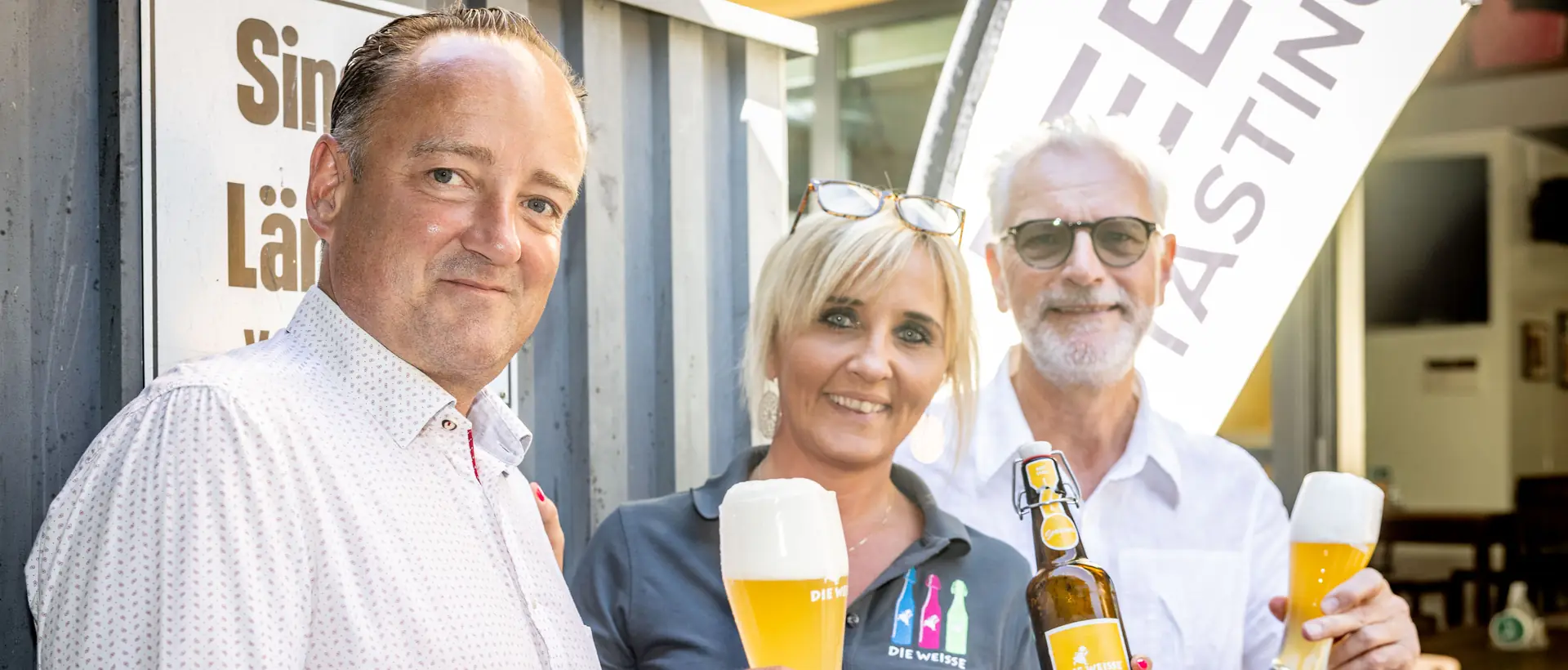 Drei Gäste stoßen vor einem Lokal mit frisch gezapftem Bier an