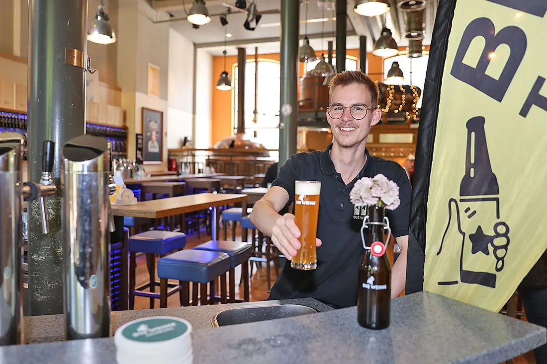 Gastronom reicht lächelnd ein frisch gezapftes Weißbier über den Tresen
